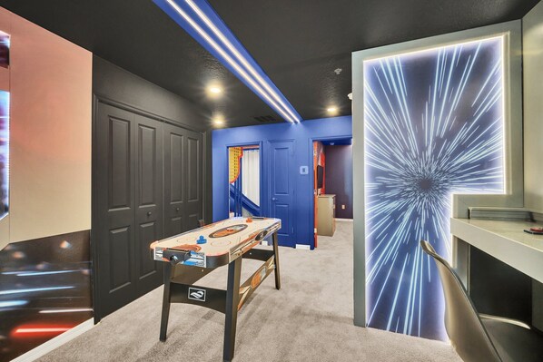 A room with a foosball table, a desk, and a wall with a light display.