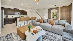 Un salon moderne avec un canapé d’angle gris, une table basse blanche et une cuisine en arrière-plan.