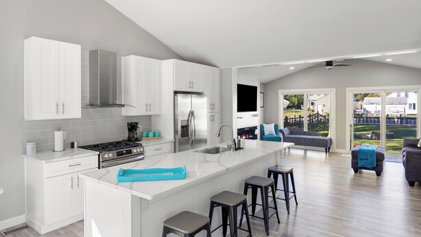 A modern kitchen with white cabinets, a central island with stools, and a large window overlooking a backyard. - Charming 3-bedroom house on the Canal! Fireplace! Firepit! Pets Welcome! (Harrison Twsp)