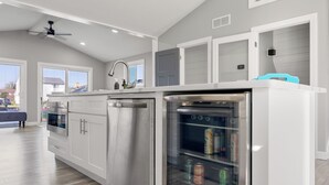A modern kitchen with white cabinetry, a built-in oven, a stainless steel refrigerator, and a glass door refrigerator containing beverages. - Charming 3-bedroom house on the Canal! Fireplace! Firepit! Pets Welcome! (Harrison Twsp)