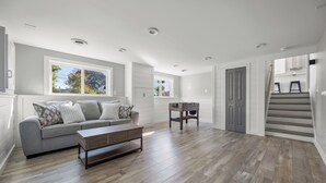 A spacious living area with a grey sofa, wooden coffee table, and a foosball table. - Charming 3-bedroom house on the Canal! Fireplace! Firepit! Pets Welcome! (Harrison Twsp)