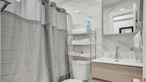 A modern bathroom with a toilet, a shower curtain, a shelf with towels, a mirror, and a sink with a faucet. - Miami Guest Suite with AC/WI-FI (North Miami Beach)