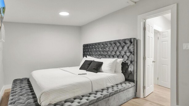 A bedroom with a tufted headboard, a bed with white bedding, and a grey upholstered bench. - Miami Guest Suite with AC/WI-FI (North Miami Beach)