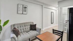 A modern living room with a grey sofa, a wooden table, and a coffee-themed wall art. - Miami Guest Suite with AC/WI-FI (North Miami Beach)