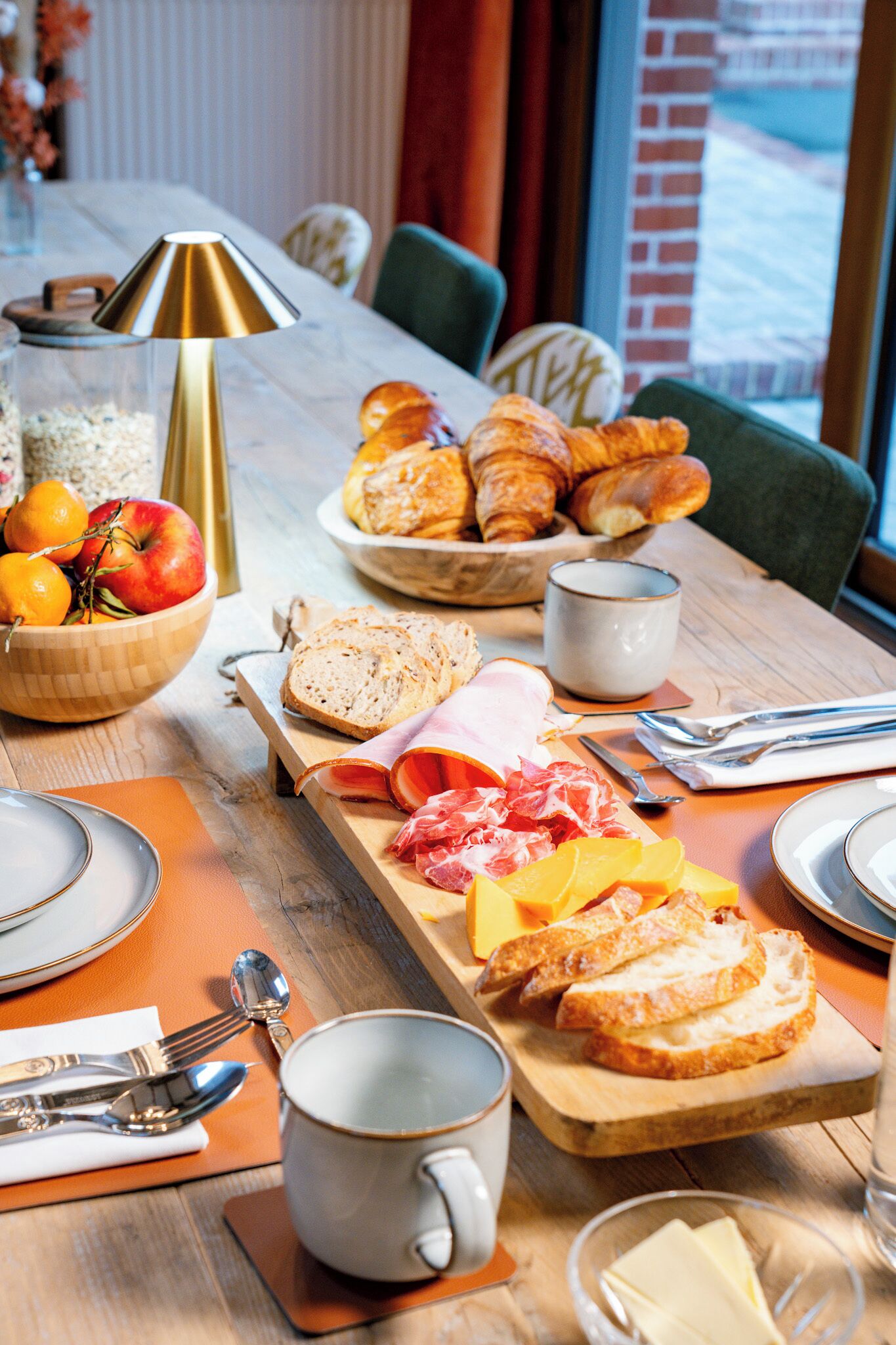 Une table de petit-déjeuner avec des croissants, du fromage, du jambon et du pain.
