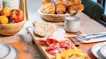Une table de petit-déjeuner avec des croissants, du fromage, du jambon et du pain.
