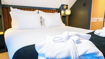 Una cama bien hecha con sábanas y almohadas blancas, cabecera de madera y una lámpara fijada a la pared.
