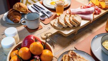 Une table de petit-déjeuner avec des croissants, des œufs, du fromage, du pain et un bol d’oranges.