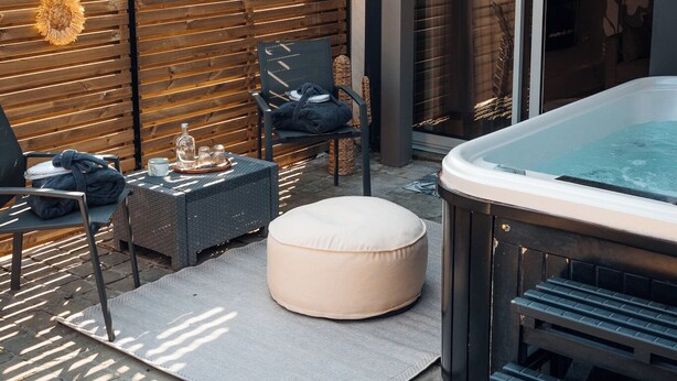 A patio area with a hot tub, seating, and a wooden wall.