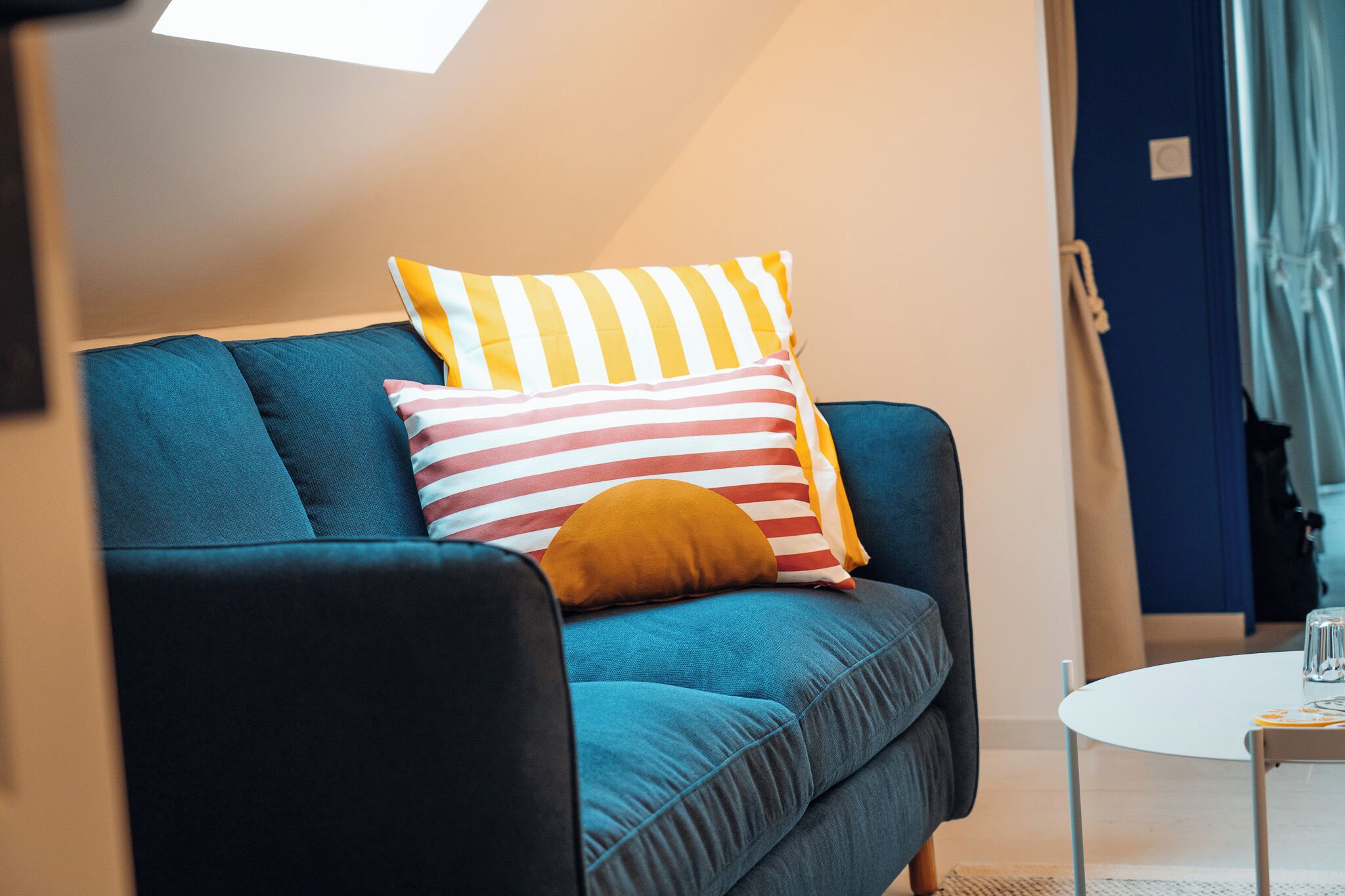 A modern living room with a blue sofa, striped pillows, and a small white table.