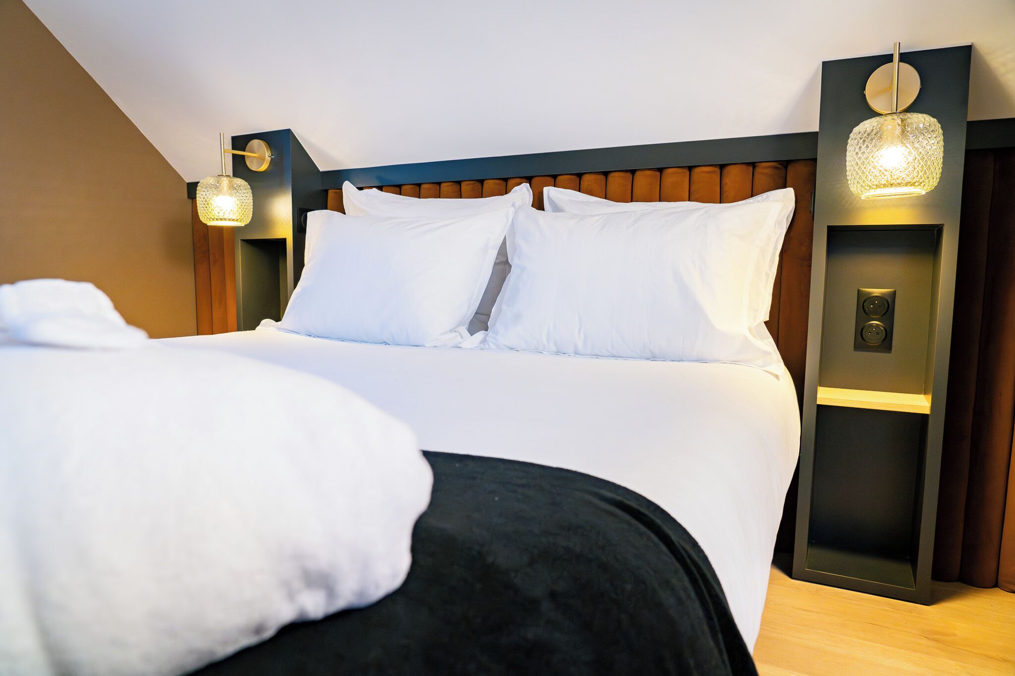 A hotel room with a large bed, two wall-mounted light fixtures, and a modern headboard.