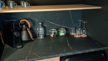 A kitchen counter with a coffee maker, a kettle, a bottle, jars, and wine glasses.