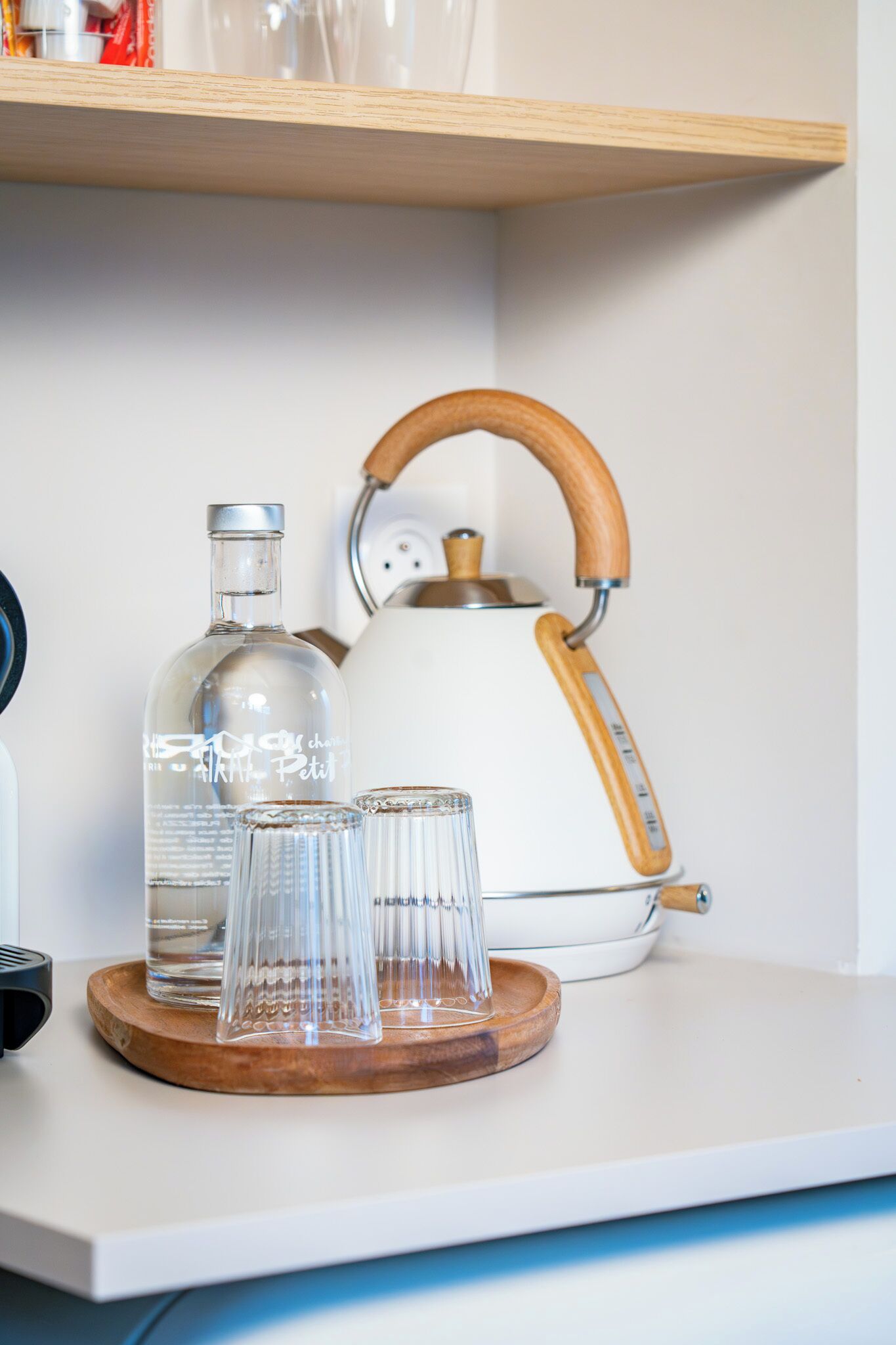 Un comptoir de cuisine avec une bouilloire, une bouteille et des verres disposés sur un plateau en bois.
