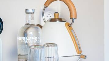 Un comptoir de cuisine avec une bouilloire, une bouteille et des verres disposés sur un plateau en bois.