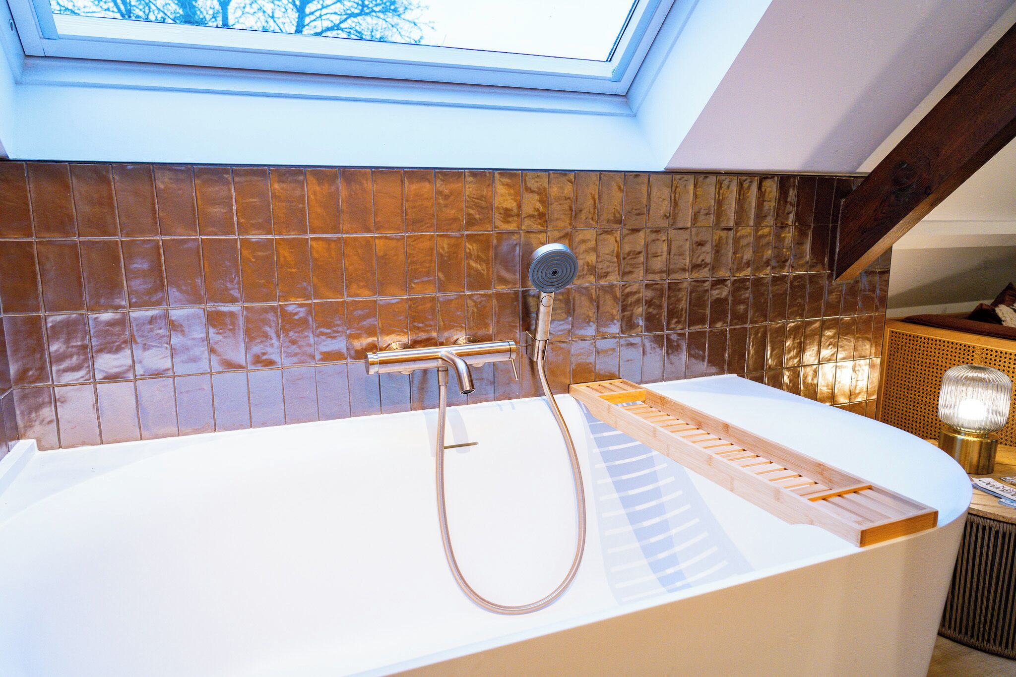 Et moderne badeværelse med ovenlys, badekar og en træhylde.
