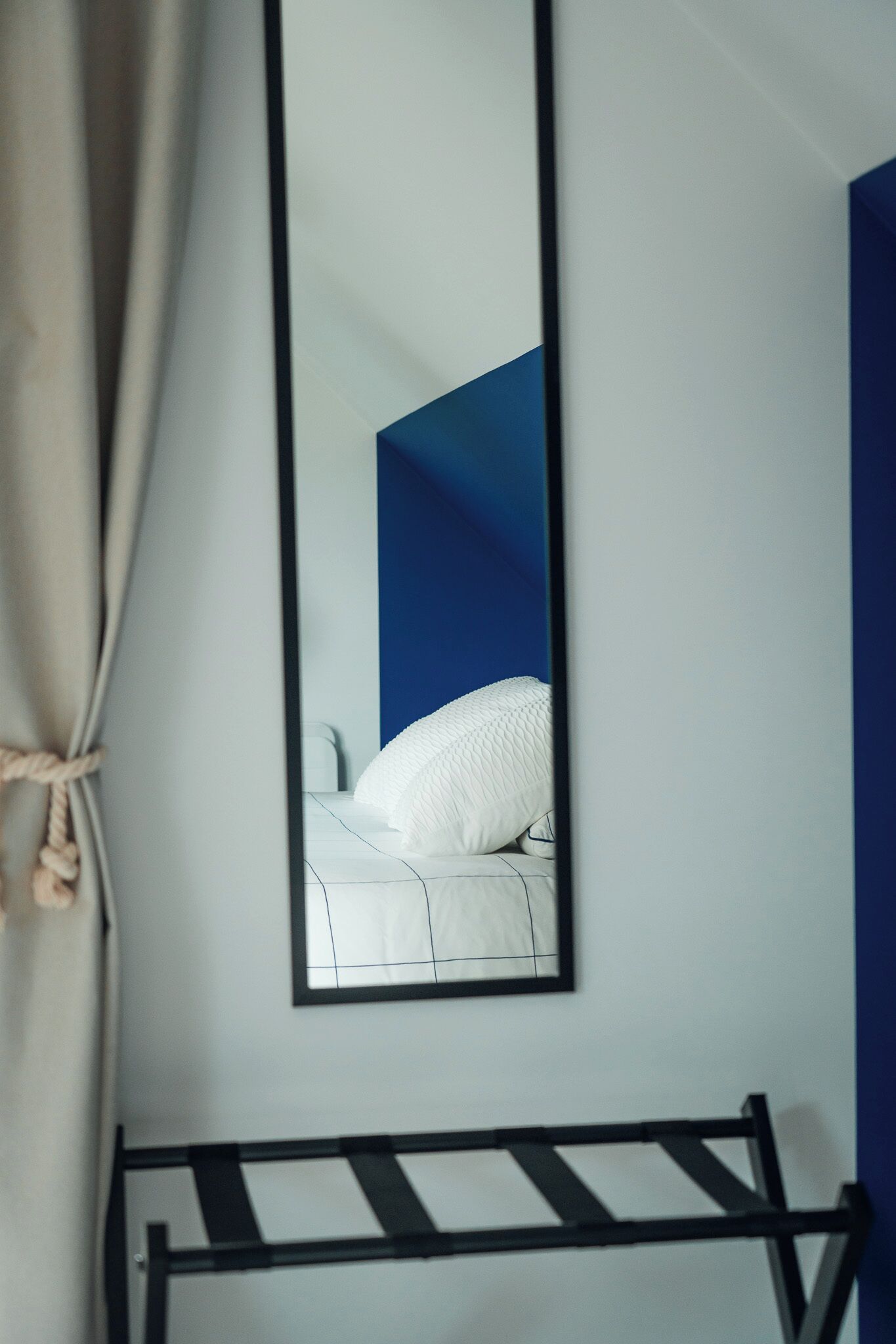 Une chambre à coucher avec un lit, un cadre en métal noir, un matelas blanc et un grand miroir qui reflète la pièce.