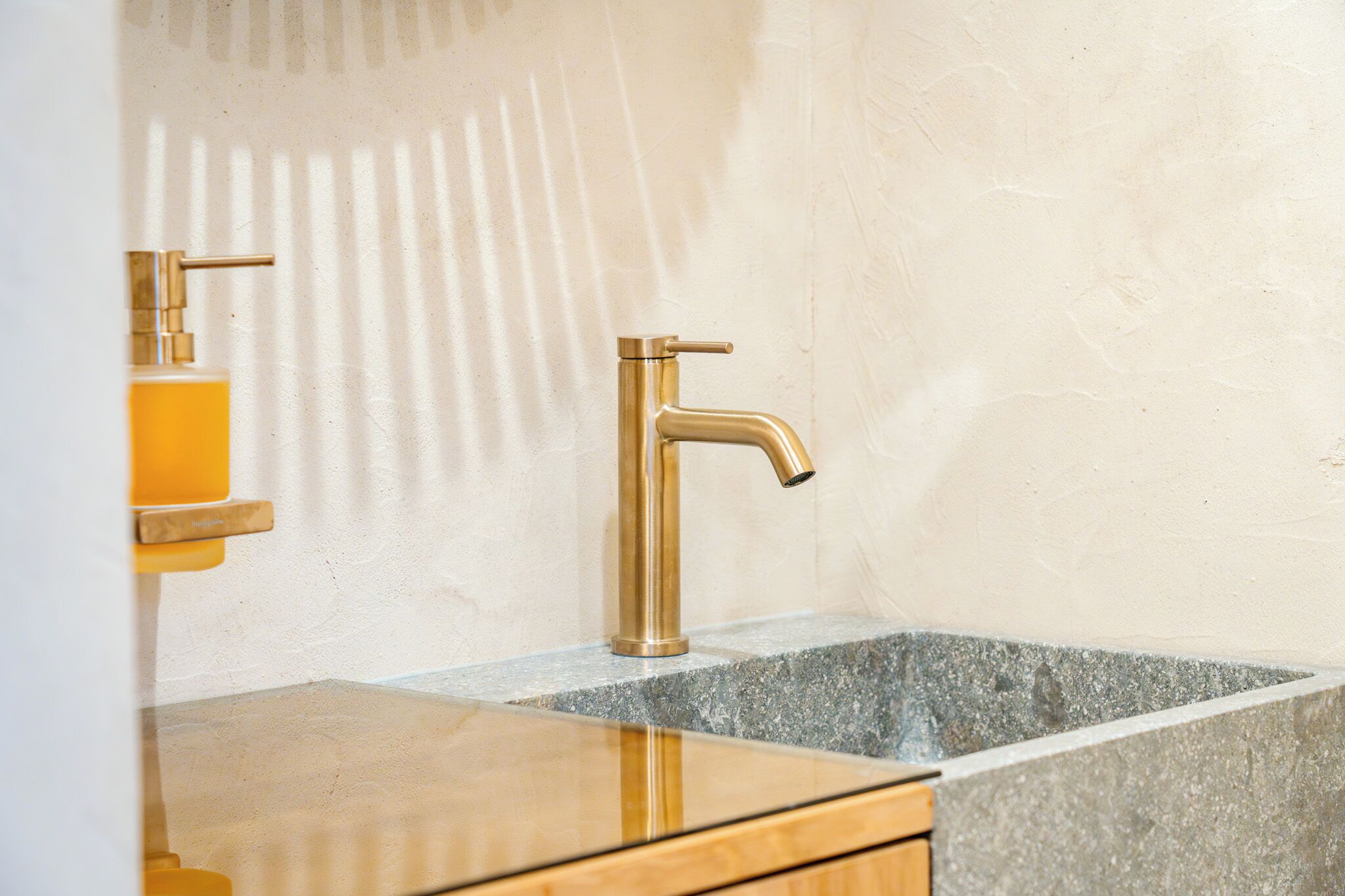 Une salle de bain avec un robinet doré, un distributeur de savon et un comptoir en granit.