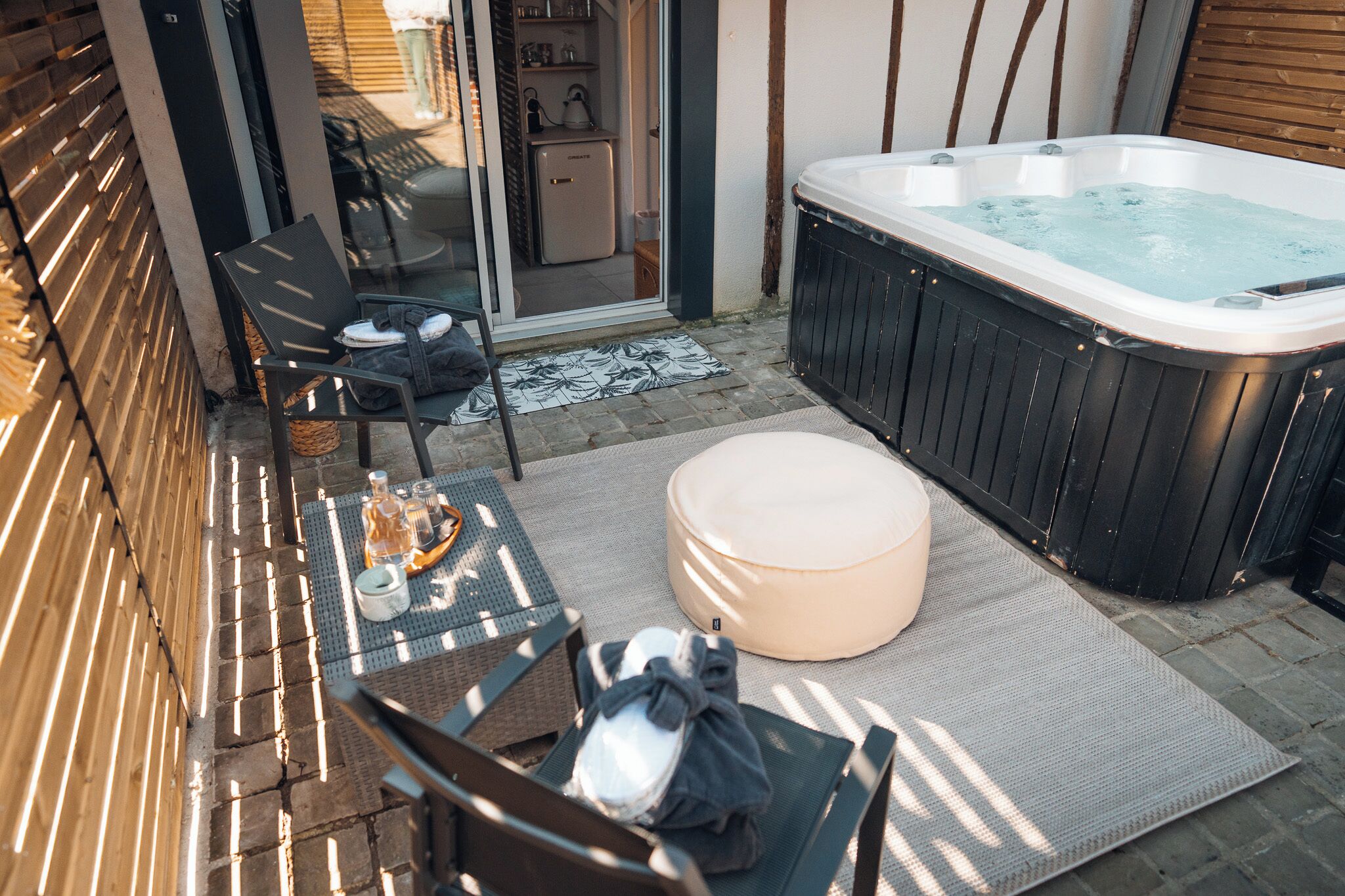 A patio area with a hot tub, outdoor seating, and a sliding glass door leading to a kitchen.