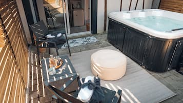 A patio area with a hot tub, outdoor seating, and a sliding glass door leading to a kitchen.