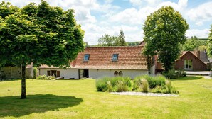 A house with a tiled roof, a garden with grass and trees, and a stone pathway.