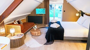 A cozy room with a bed, a sofa, a TV, and a small table with a lamp.