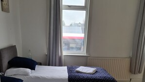 A double room with two beds, a window with curtains, a radiator, and a view of a red building outside. - Cosy 4 bed house in great location. (London)