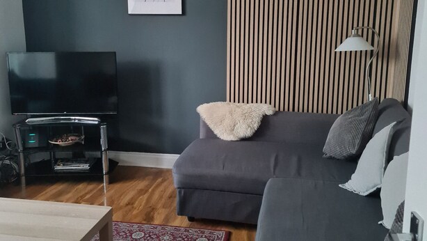 A modern living room with a grey sofa, a flat-screen TV, a wooden floor, and a patterned rug. - Cosy 4 bed house in great location. (London)