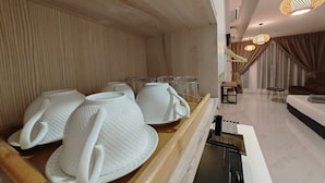 A modern hotel room with a wooden wall, a dining area with white ceramic tableware, and a cozy seating area with a sofa and curtains.