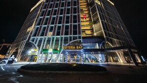 A modern hotel with a prominent 'Suteria Bay' sign, multiple floors, and a well-lit facade.
