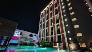 A modern hotel with a swimming pool, a well-lit facade, and a sign indicating "Borneo Housing".