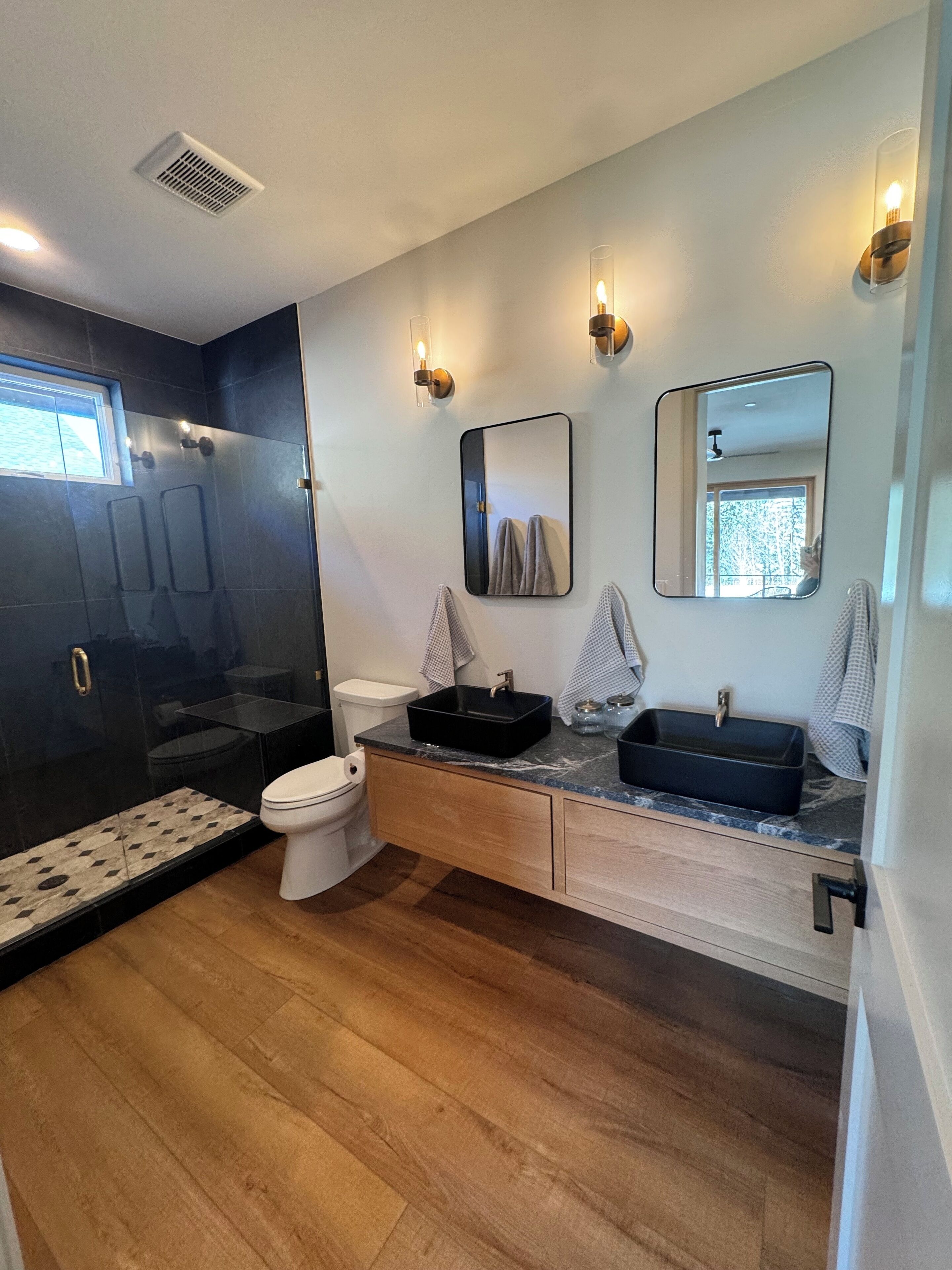 A modern bathroom with a glass shower enclosure, a white toilet, a black sink, and a mirror.