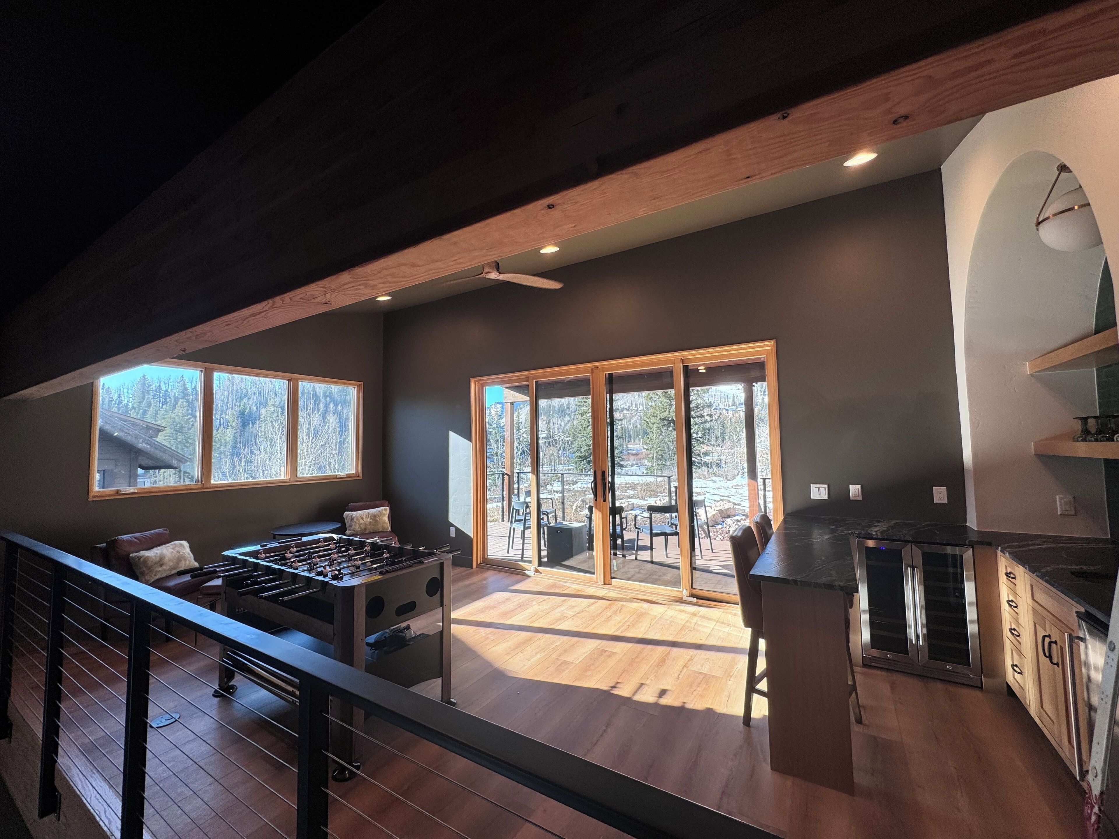 A spacious living area with a wooden ceiling, a foosball table, and a large sliding glass door leading to an outdoor patio.