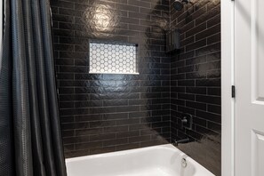 Ein Badezimmer mit schwarzen Fliesenwänden, einer weißen Badewanne und einer Duschbrause.