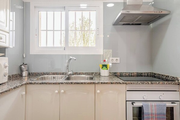 A kitchen with a granite countertop, stainless steel sink, and a stove.