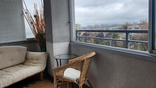 Un balcón con sofá, una silla de mimbre y una mesa de vidrio.