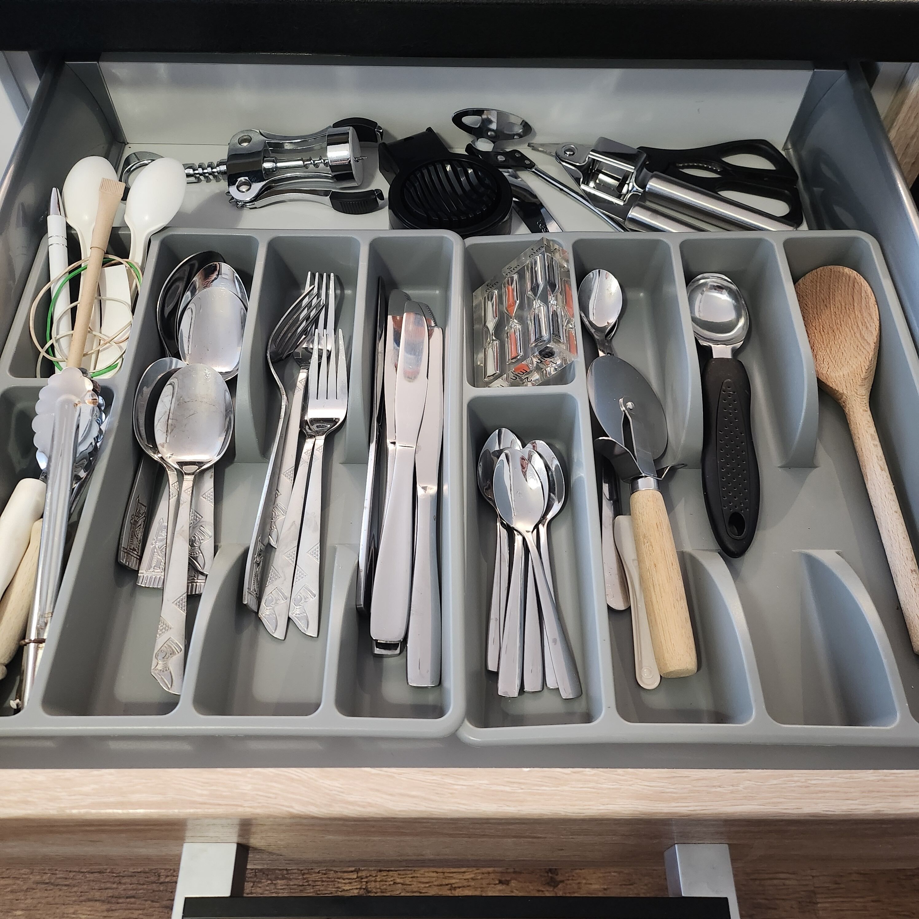 Un cajón con varios compartimentos que contiene distintos utensilios de cocina, como cucharas, tenedores, cuchillos y un rallador.