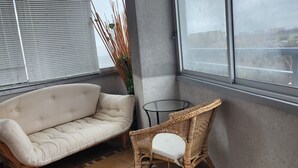Un balcón con sofá, una silla de mimbre y una mesita.