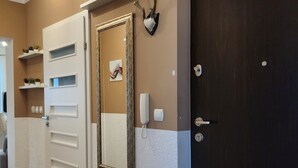 Un pasillo con una puerta blanca, una puerta oscura, un teléfono en la pared y un espejo enmarco.