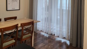 Un comedor con una mesa y sillas de madera, una obra de arte enmarcada en la pared y cortinas translúcidas con un estampado a rayas.