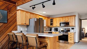 A modern kitchen with wooden cabinets, a stainless steel refrigerator, a microwave, and a large island with bar stools. - Cozy 6-bedroom cabin in Wintergreen Resort (Wintergreen Resort)