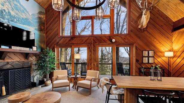 A cozy cabin interior with a fireplace, comfortable seating, and large windows offering views of the surrounding forest. - Cozy 6-bedroom cabin in Wintergreen Resort (Wintergreen Resort)