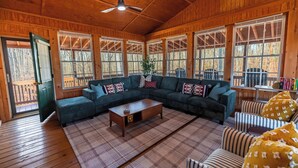 A cozy cabin interior with a large sectional sofa, a wooden coffee table, and a ceiling fan.
