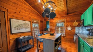 A wooden cabin interior with a dining area, kitchen, and a framed map on the wall.
