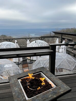 A rooftop terrace with a fire feature, covered seating areas, and a view of a lake and distant landscape.