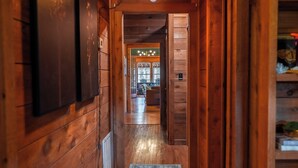 A wooden hallway with a patterned rug leading to a room with a green wall and a chandelier.