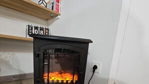 Ein schwarzer Holzofen mit Glastür, ein Regal darüber und eine weiße Wand im Hintergrund.