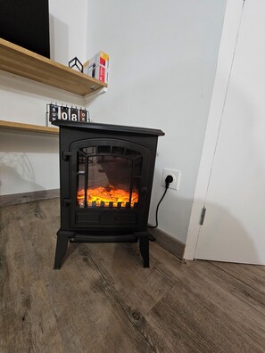 A black wood-burning stove with a glass door, a shelf above it, and a white wall in the background.