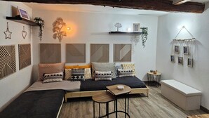 Ein gemütlicher, hell eingerichteter Raum mit Holzboden, einer Couch mit gemusterten Kissen, einem kleinen Tisch und Wanddekorationen.