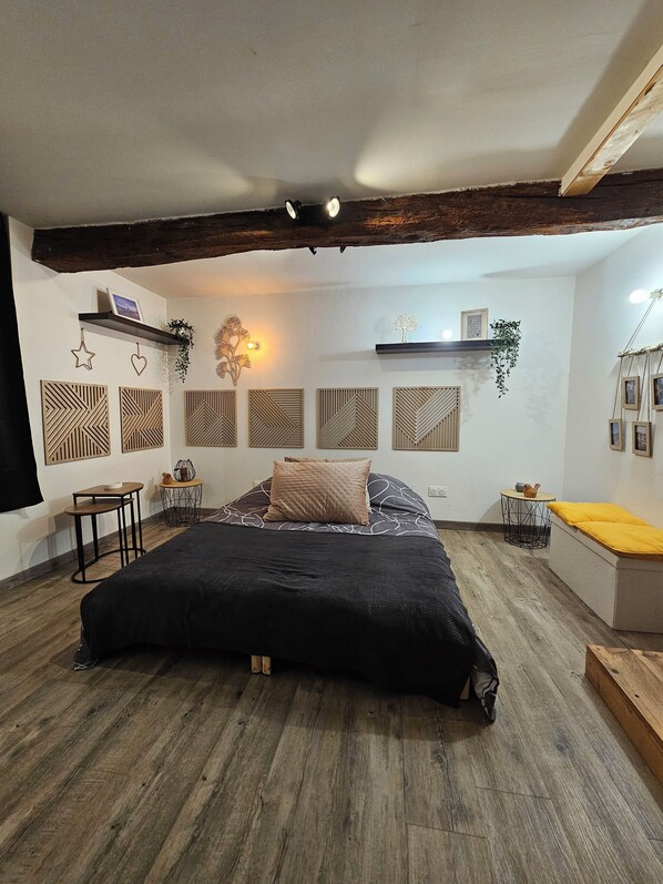 A bedroom with a large bed, wooden flooring, and a sloped ceiling with exposed beams.