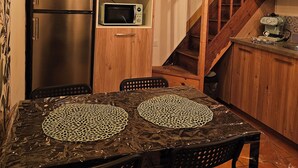 Eine rustikale Küche mit Holzschnitzschränken, einem Edelstahlkühlschrank, einer Mikrowelle und einem Tisch mit zwei Untersets.